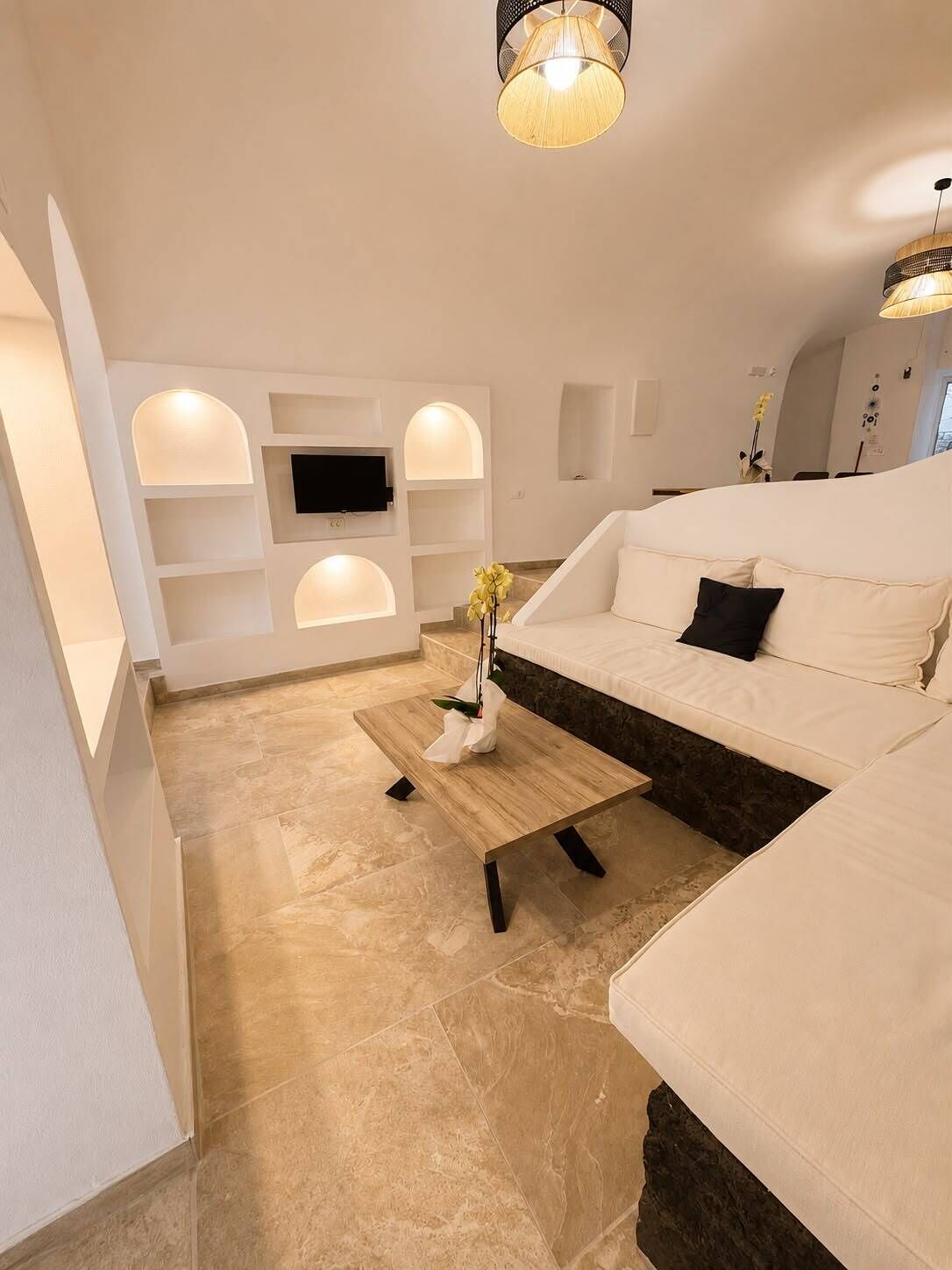 Ein modernes Wohnzimmer mit einem weißen Sofa, einem Couchtisch und einem an der Wand befestigten Fernseher.