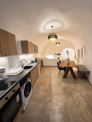A compact kitchen with a washing machine, a dining area with a bench, and a hanging light fixture.