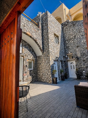Un patio con muros de piedra, una puerta de madera y mobiliario exterior.