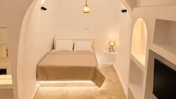 A bedroom with a curved ceiling, a bed with a beige cover, a wall-mounted TV, and a small bedside table with a lamp.
