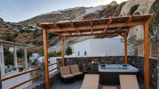 Área externa com assentos, uma pérgola de madeira, duas poltronas de descanso, uma mesa pequena e uma banheira de hidromassagem.