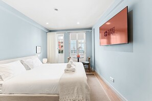 A hotel room with a bed, a TV mounted on the wall, and a view of the outside through a window. - GuestReady - City centre stay in Porto (Porto)