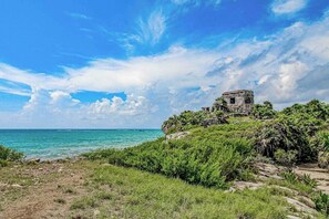 A coastal landscape with a stone structure on a hill, overlooking the sea. - Beachfront home pool, chef, transport (Tulum)