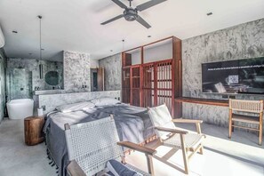 A modern bedroom with a bed, a desk, a television, and a seating area. - Beachfront home pool, chef, transport (Tulum)