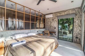 Een slaapkamer met een groot bed, een bureau en uitzicht op een tropisch buitengebied.