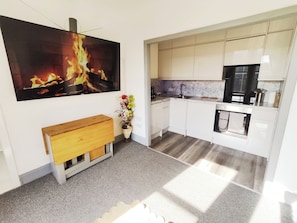 Een moderne keuken met witte kasten, een houten bankje, een groot schilderij van een vuur, en een vaas met bloemen.