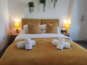 Een hotelkamer met een bed, twee nachtkastjes, een lamp, een klok en een plant aan de muur.