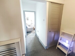 Ein Flur, der zu einem Schlafzimmer mit Babybett, Heizkörper und weißem Regal führt.