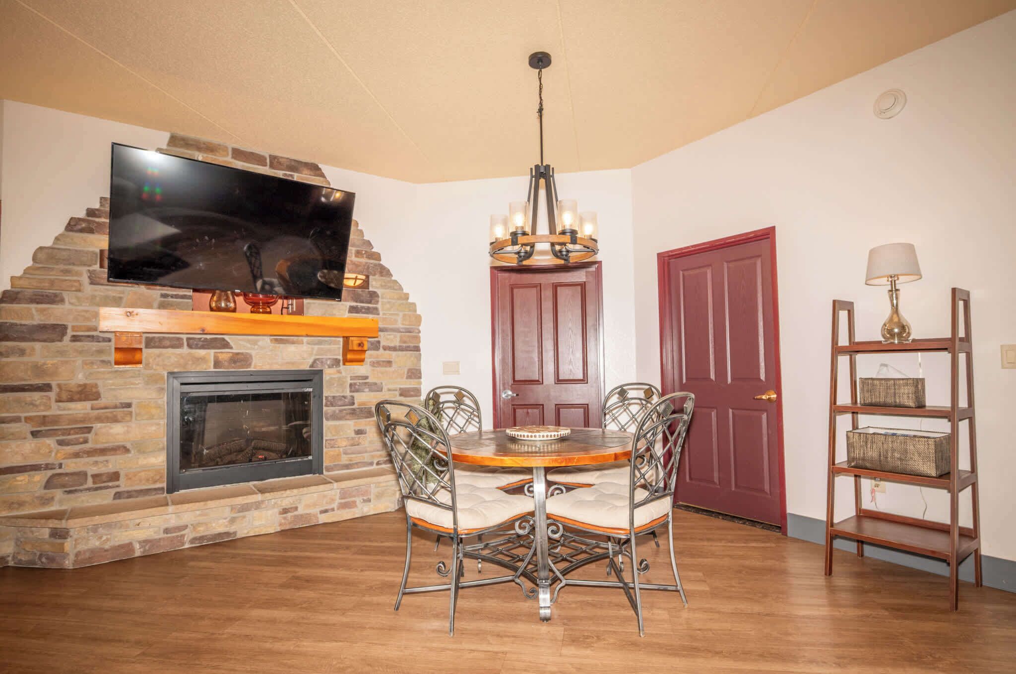 A dining area with a brick fireplace, a flat-screen TV, a chandelier, and a red door.