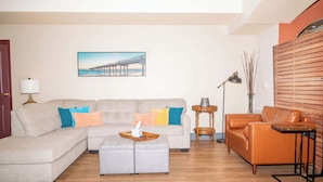 A living room with a sofa, ottoman, and a coffee table. There is a painting on the wall and a lamp on a side table. - Chula Condo 2237 & 2239 (Wisconsin Dells)