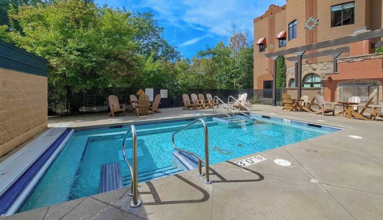 Una piscina con sillas de descanso y un edificio al fondo.
