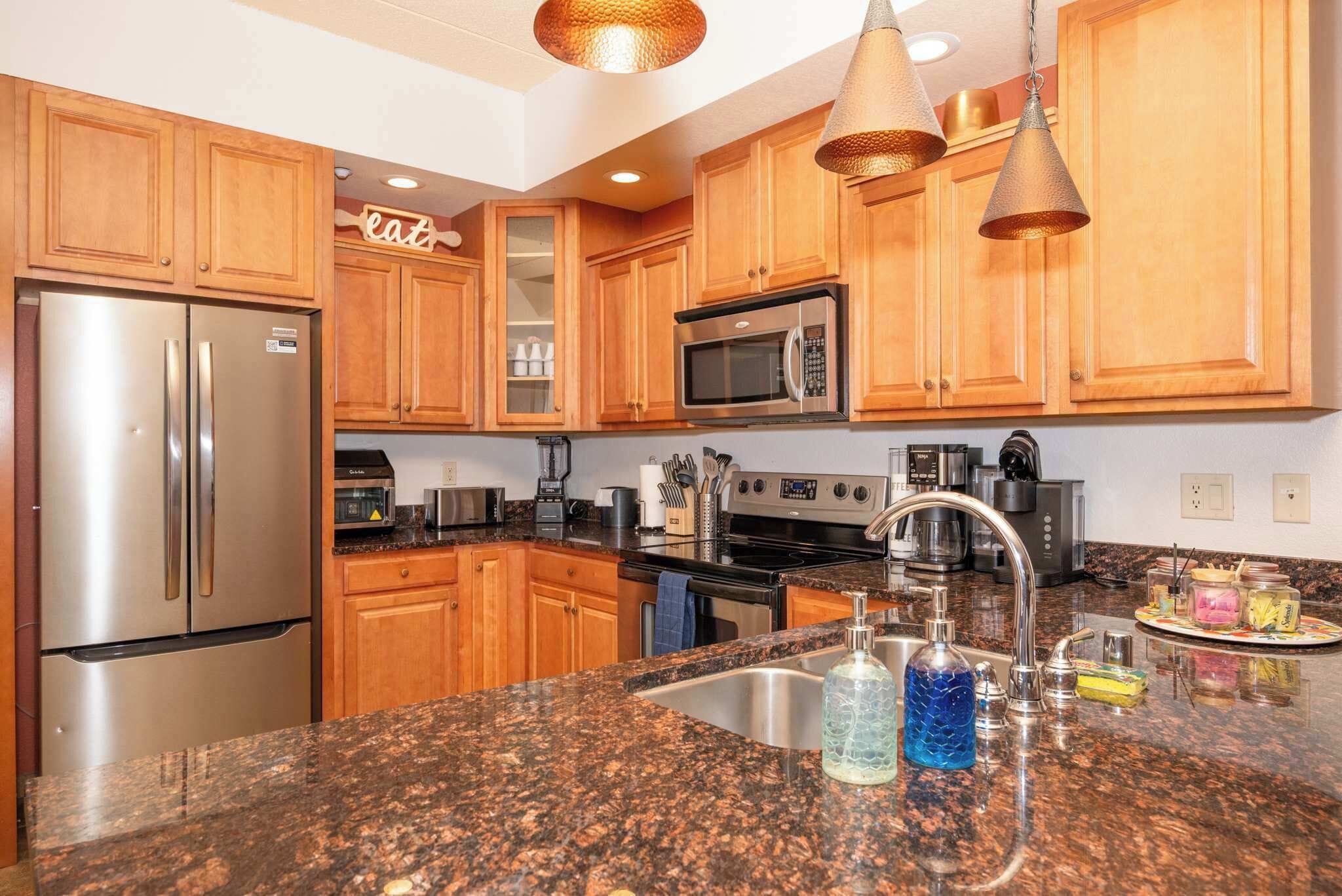 A kitchen with wooden cabinets, stainless steel appliances, granite countertops, and pendant lighting.