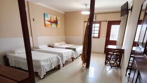 A hotel room with two beds, a wooden chair, a table, a painting on the wall, and a window with curtains. - Pousada Praia Grande (Fundão)