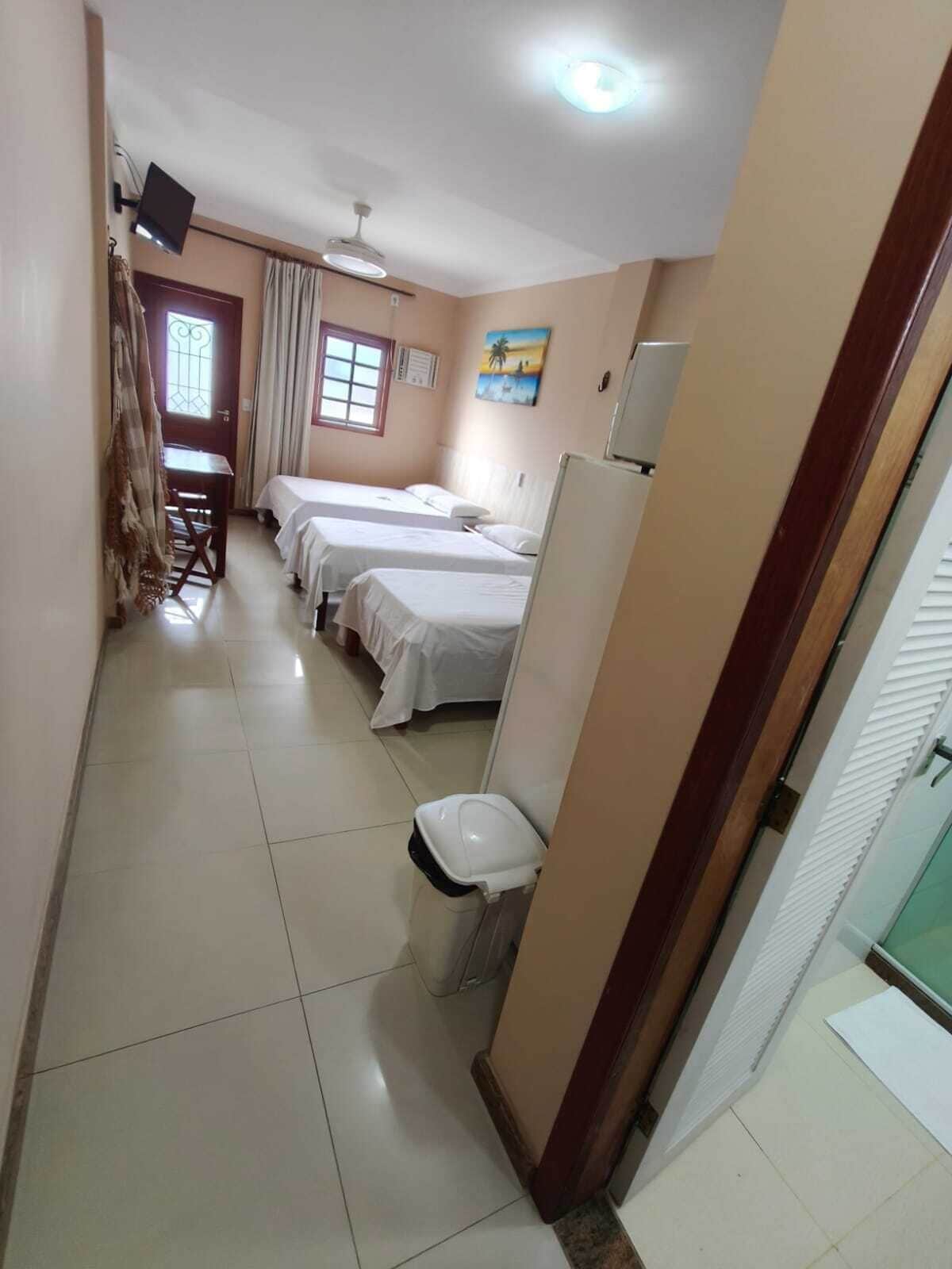 Habitación de hotel con dos camas, un escritorio, una silla, una ventana, un ventilador de techo y un inodoro.