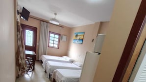 A hotel room with two beds, a desk, a chair, a window, a ceiling fan, and a toilet. - Pousada Praia Grande (Fundão)