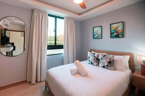 A hotel room with a bed, a round mirror, two paintings, and a window with curtains. - NOK Stylish 2BR Retreat at Residences Vistacana (Punta Cana)