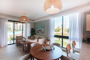 Ein modernes Wohnzimmer mit einer Couch, Sesseln, einem Esstisch und Blick auf einen Swimmingpool und Gebäude.