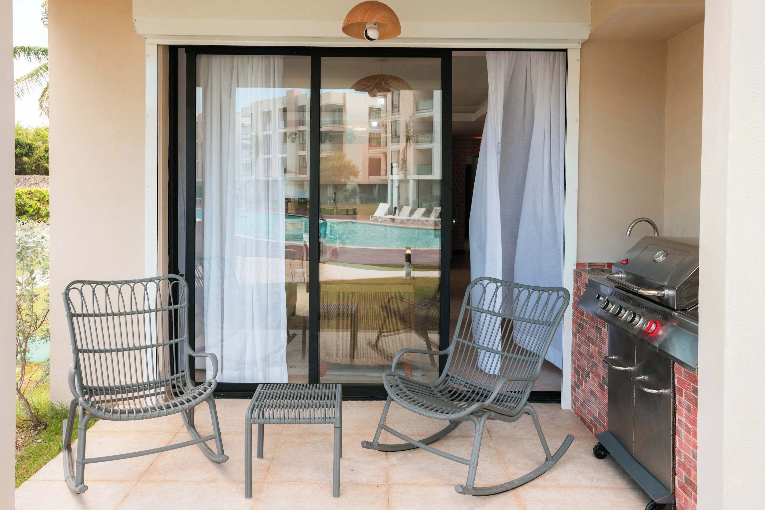 Un balcon avec deux fauteuils à bascule, un barbecue et une vue sur une piscine et des immeubles.