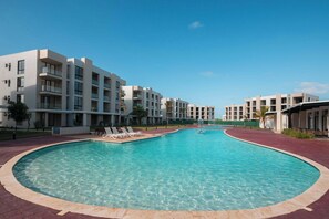 Ein modernes Hotel mit einem zentral gelegenen Pool, mehreren Balkonen und wolkenlosem, blauem Himmel.