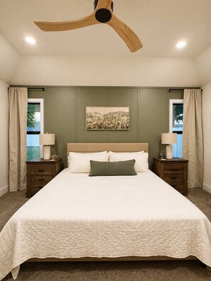 A bedroom with a large bed, two bedside tables, a ceiling fan, and a window with curtains. - Rave On Retreat - 3BR/2BA - Family Friendly (Lubbock)