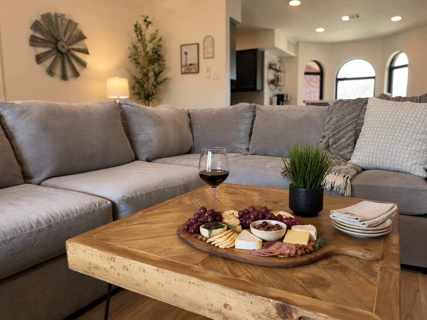 A living room with a wooden coffee table displaying a charcuterie board, a glass of red wine, and a potted plant.