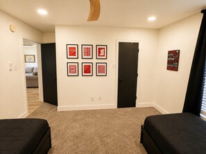 A hotel room with two beds, a carpeted floor, a door, and a wall with framed pictures. - Rave On Retreat - 3BR/2BA - Family Friendly (Lubbock)