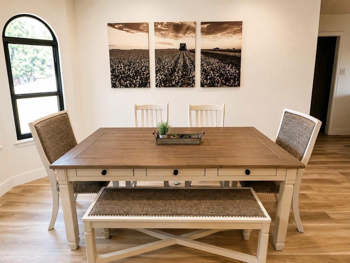 A dining area with a wooden table, four chairs, a bench, and three wall-mounted paintings.