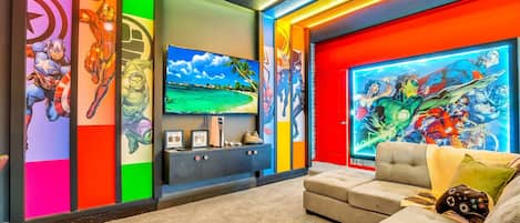 Una sala moderna con un televisor de pantalla plana grande, un sofá y llamativos murales con temática de cómics.