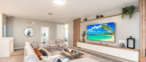 Una sala de estar moderna con un televisor de pantalla plana grande, un sofá, una mesa de centro y un comedor.