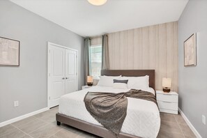 Ein Schlafzimmer mit einem Bett, Nachttischen, einem Fenster mit Vorhängen und einer Tür.
