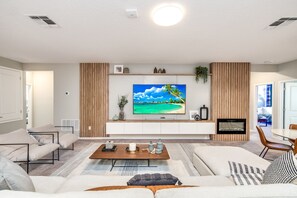 Een moderne woonkamer met een flatscreen televisie, een bank, een salontafel en een eethoek.