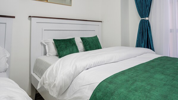 A neatly made twin bed with white and green bedding, a wooden headboard, and a window with teal curtains. - 2-bedroom apartment with three beds in charming westlands-Nairobi (Nairobi)
