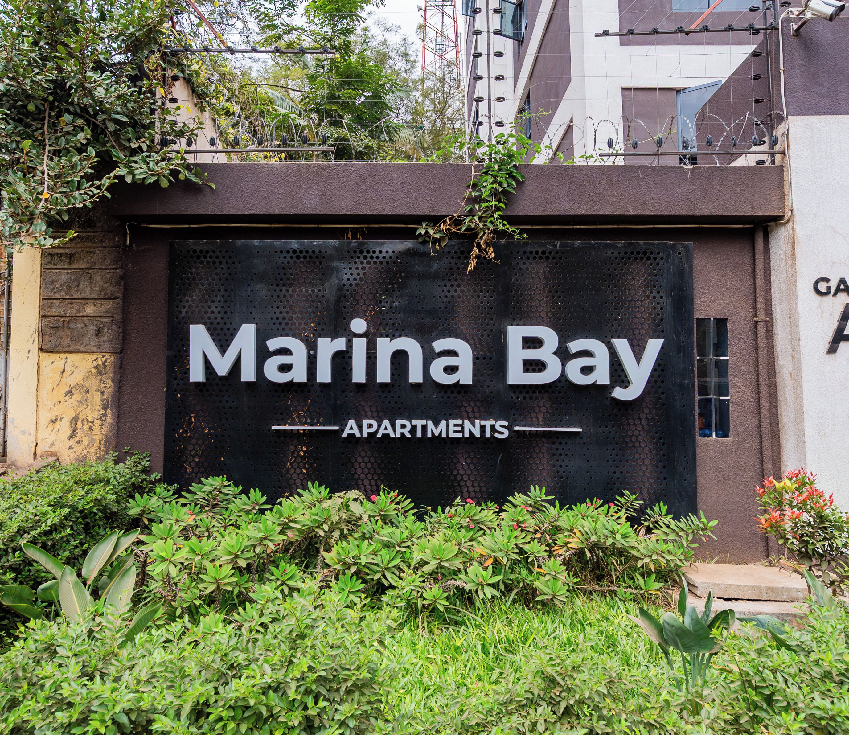 Een bordje voor 'Marina Bay Apartments' met een modern ontwerp en beplanting ervoor.