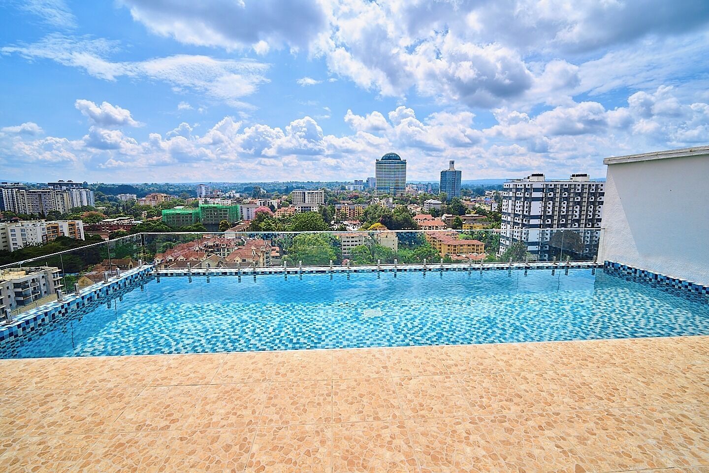 A rooftop swimming pool with a view of a cityscape, including high-rise buildings and a clear sky.