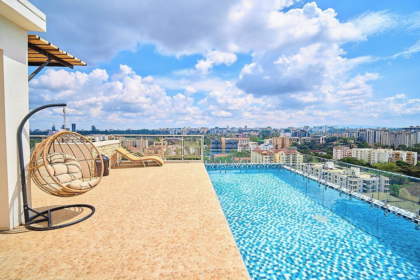 A rooftop pool with a city view, a hanging chair, and a sun lounger.