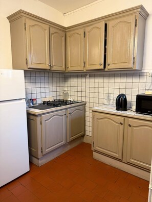 Una cucina con mobili beige, un frigorifero bianco, un piano cottura a gas, un forno a microonde e uno schienale piastrellato.