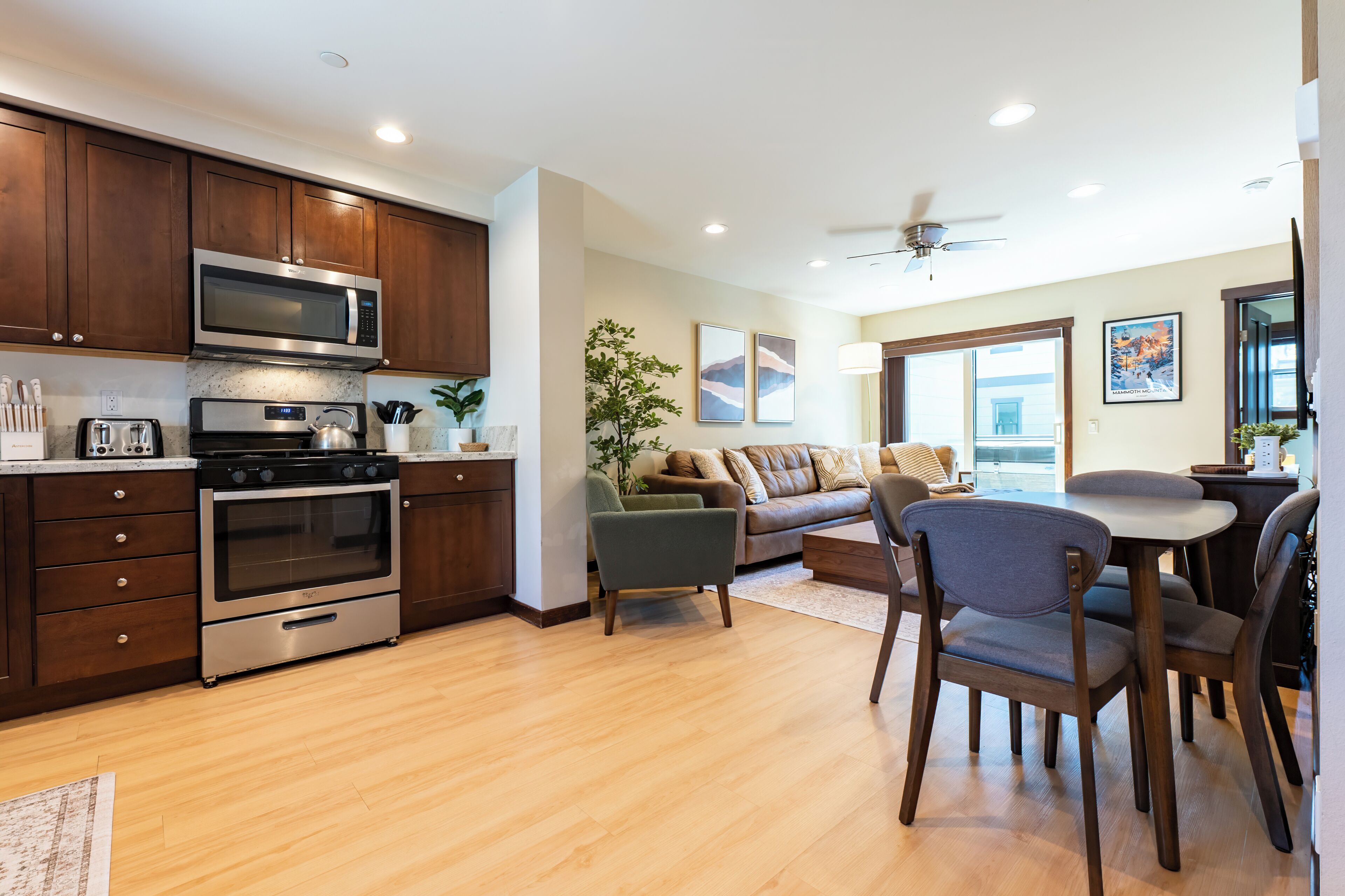 Cozinha moderna com eletrodomésticos embutidos, área de jantar com mesa e cadeiras, e sala de estar com sofá e ventilador de teto.