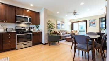Cozinha moderna com eletrodomésticos embutidos, área de jantar com mesa e cadeiras, e sala de estar com sofá e ventilador de teto.
