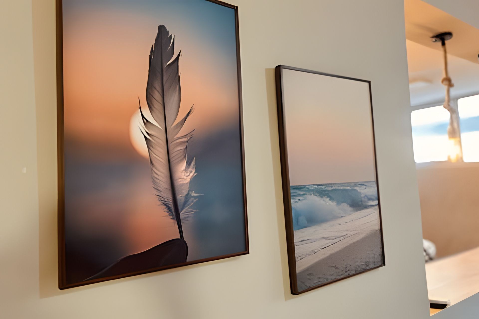 Two framed artworks on a wall, one depicting a feather and the other a beach scene.