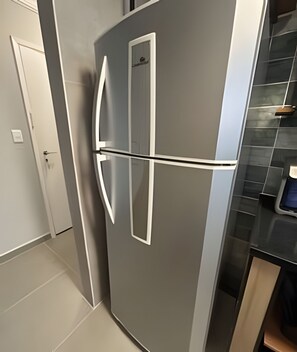 A modern kitchen with a stainless steel refrigerator, a white door, and a tiled backsplash.