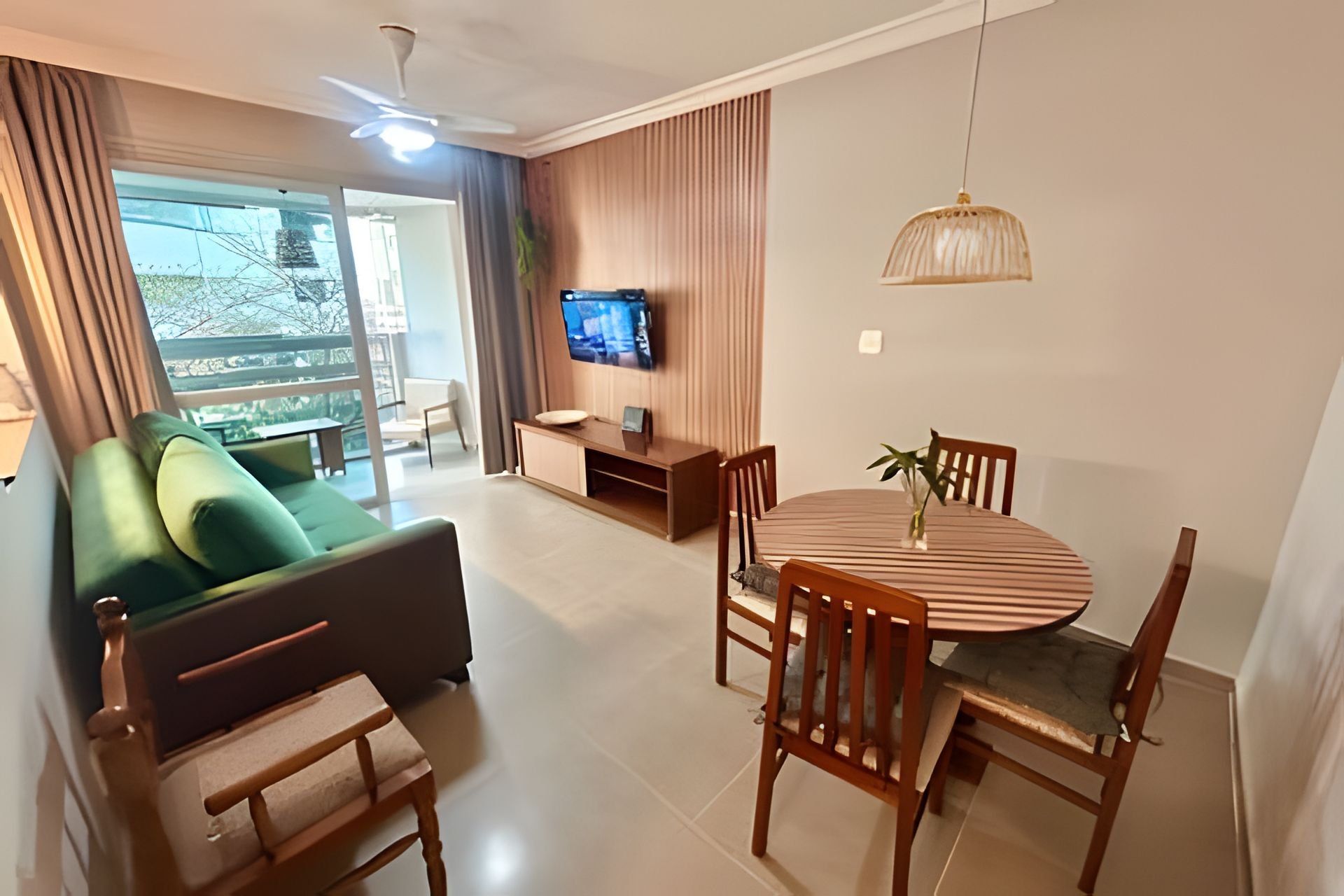 Een moderne woonkamer met een bank, een eettafel met stoelen, een televisie aan de muur en een plafondventilator.