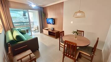 Een moderne woonkamer met een bank, een eettafel met stoelen, een televisie aan de muur en een plafondventilator.