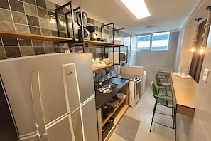 A modern kitchen with a built-in oven, a sink, and a dining area with a chair. - SHB - O Melhor de Pitangueiras  (Guarujá)