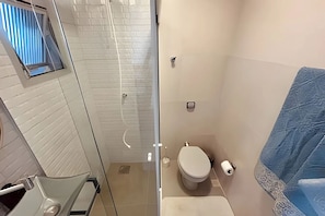 A bathroom with a glass shower enclosure, a toilet, and a towel rack. - SHB - O Melhor de Pitangueiras  (Guarujá)