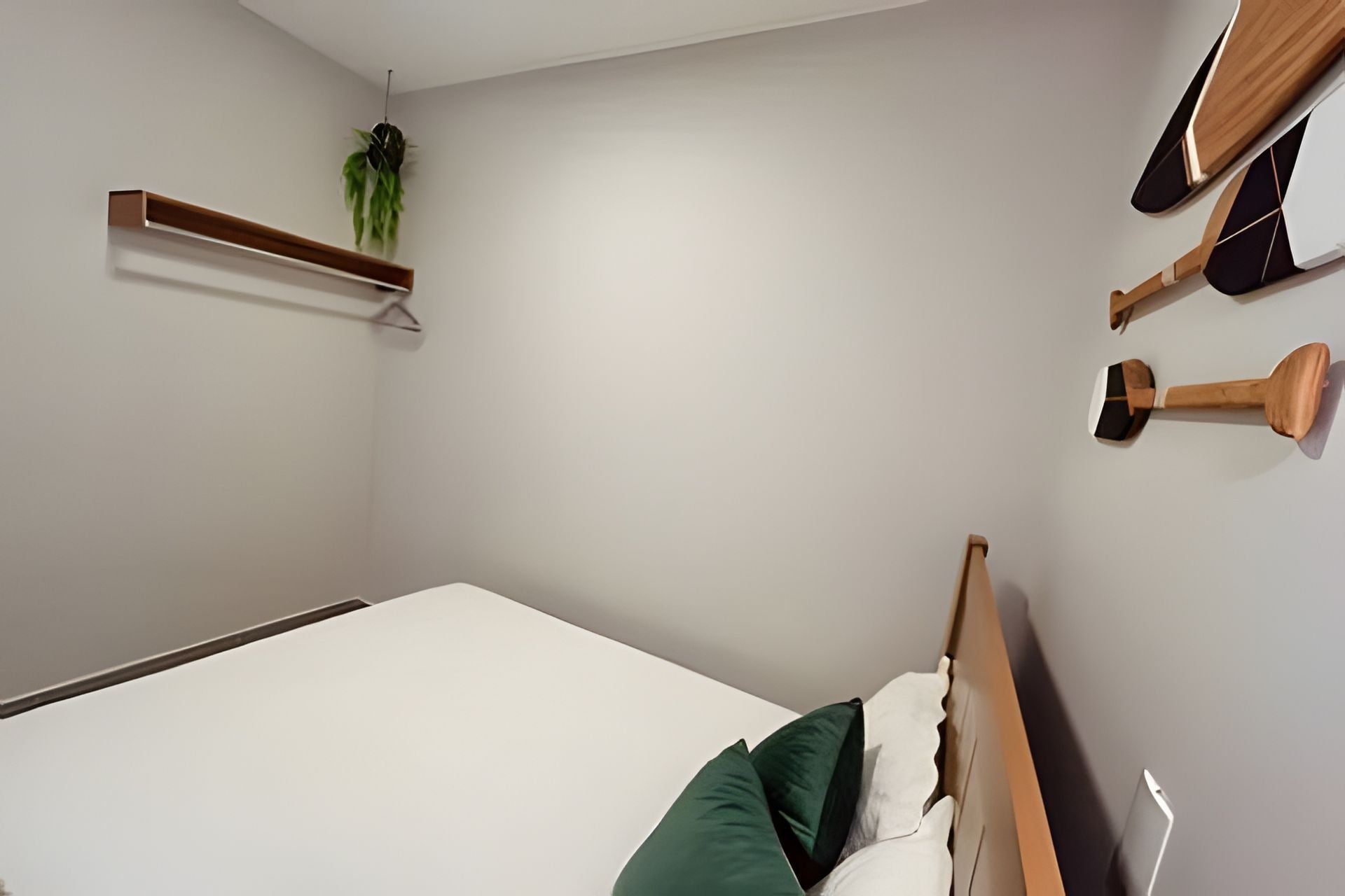 A bedroom with a bed, a wooden headboard, a shelf with a plant, and a wall-mounted wooden object.
