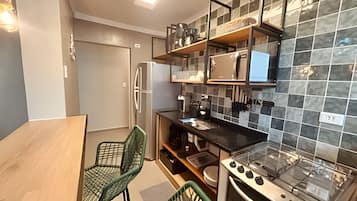 Een praktische keuken met een koelkast, fornuis en een kleine eethoek met stoelen.