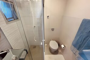 Un baño con cabina de ducha de vidrio, inodoro y toallero.
