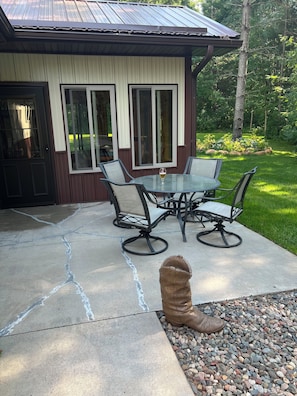 A patio with a glass table and chairs, a concrete floor with cracks, and a small statue of a bear. - Bikers retreat (Deerwood)