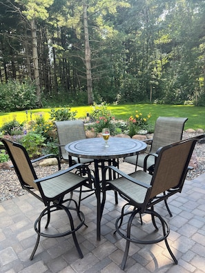 A round outdoor table with four chairs, surrounded by a garden with various plants and flowers. - Bikers retreat (Deerwood)