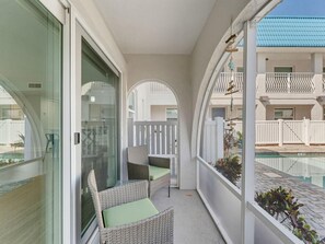 A balcony with wicker chairs and a glass door, overlooking a swimming pool and a building with balconies. - El Mar Condos #113 - "three Sisters" (North Redington Beach)